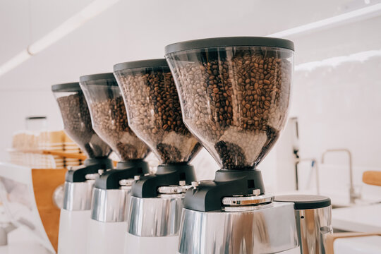 Row of professional coffee grinders filled with roasted coffee beans, ready for espresso and brewing in a contemporary cafe