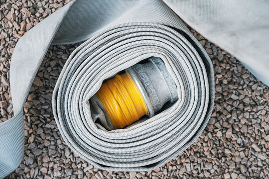 Rolled fire hose with a yellow and metal coupling, placed on an outdoor gravel surface for emergency preparedness