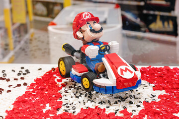 Naklejka premium 14 January 2026, Dubai, UAE: Lego Super Mario figure in a brick built kart, surrounded by loose red and white building blocks, illustrating creativity and play