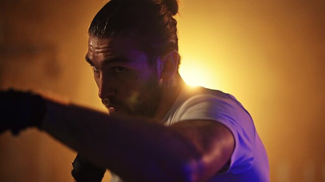Determined male boxer training with punching combinations in a smoky, dark gym with dramatic backlighting
