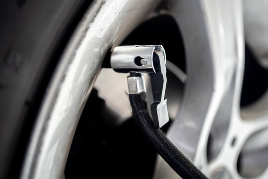 Detailed close-up of an air pump nozzle connected to a car tire valve on an alloy wheel - concept of vehicle maintenance, tire inflation and safety check