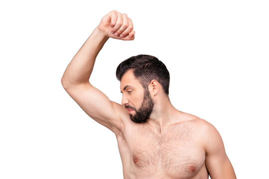 Close up portrait of man with bristle, smelling his armpit, feeling bad odor, wants to take a shower, has a bad body cosmetic, needs antiperspirants, standing over grey background