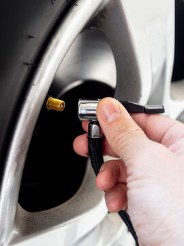 Close-up of a hand connecting an air pump to a car tire valve on an alloy wheel - concept of vehicle maintenance, tire inflation and safety check