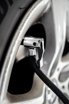 Detailed close-up of an air pump nozzle connected to a car tire valve on an alloy wheel - concept of vehicle maintenance, tire inflation and safety check