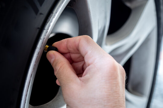 Close-up of a hand screwing a cap onto a car tire valve on an alloy wheel - concept of vehicle maintenance, tire inflation and safety check