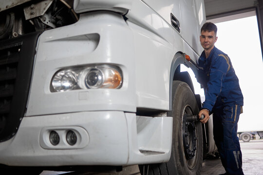 A confident mechanic diligently working on a truck, expertly unscrewing a wheel with a professional tool. The image showcases their skill and focus in a well-equipped garage.