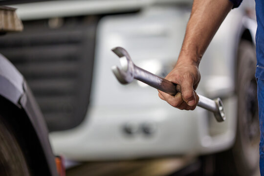 An experienced mechanic wearing blue overalls passionately showcases his repair skills while holding a wrench. The image captures the essence of automotive maintenance and expertise.