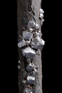 Zinc crystal cluster on dark mineral rod with metallic reflection and rough texture, abstract macro mineral specimen on black background