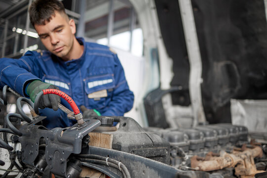 In this close-up scene, a skilled mechanic in a blue uniform specializes in performing important maintenance tasks under the hood of a truck, ensuring its reliability and safety for daily journeys.