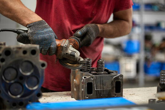 A mechanic diligently cleaning a truck cylinder head with a grinder in a well-lit, professional garage. The scene captures the precision and tools of automotive repair.