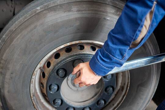 This image features a professional mechanic at a service shop, expertly unscrewing a truck wheel. His focus and usage of a large tool emphasize the intricate work involved in automotive maintenance.