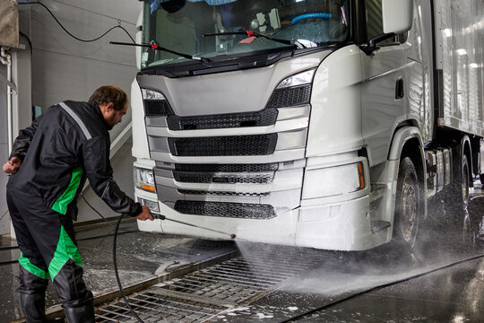 .Inside a spacious car wash, a focused cleaner meticulously cleans the interior of a shiny white truck cabin, ensuring every detail sparkles. Bright lighting highlights the professional atmosphere.