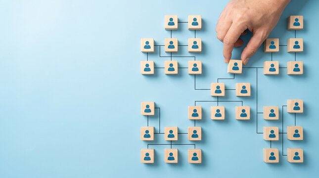 Hand placing a wooden block with a person icon into a hierarchical organizational chart on a blue background, symbolizing team building and hr