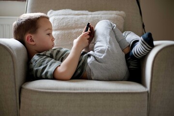Obraz premium Child young boy using smartphone playing game relaxed at home
