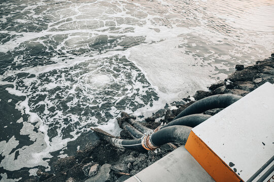 Polluted water with thick foam flowing out of multiple industrial drainage pipes into a body of water, causing environmental damage