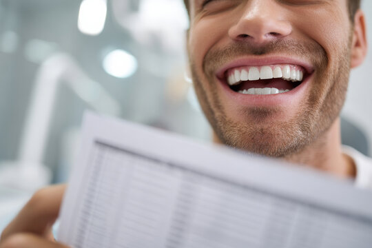 Smiling man showing straight teeth while dentist examines dental chart beside him, modern dental clinic background softly blurred, bright professional lighting concept for corporate