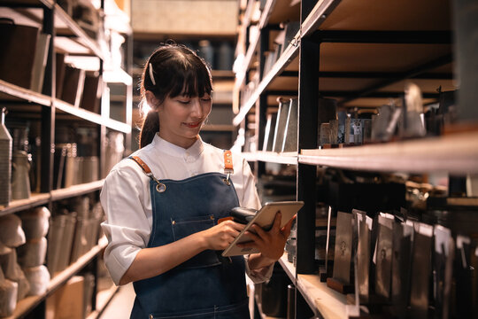 Young woman using tablet in warehouse aisle, inventory check in storage room with shelf and package