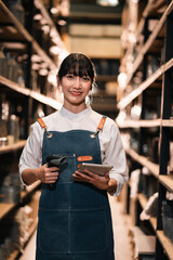 Smiling woman holding tablet and scanner in warehouse aisle, inventory worker in apron and white shirt, industrial storage and logistics © chokniti