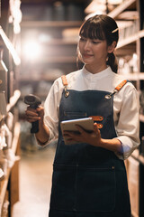 Woman warehouse worker using scanner tablet young asian woman in apron checking inventory in storage aisle female employee in logistics stockroom with handheld device © chokniti