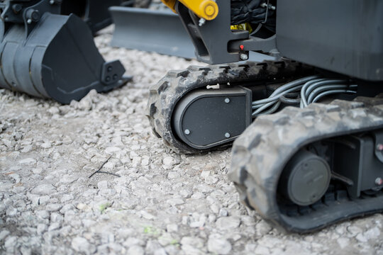 Compact excavator rubber track and undercarriage on gravel with hydraulic hoses, bucket and blade attachments in a construction rental yard setting