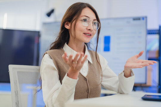 professional female software developer with glasses sitting at her desk, holding a coffee cup while intently working on her laptop. The scene captures a modern business environment 