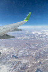 Obraz premium The visible part of an airplane wing over snow-capped mountain peaks. Airplane flight