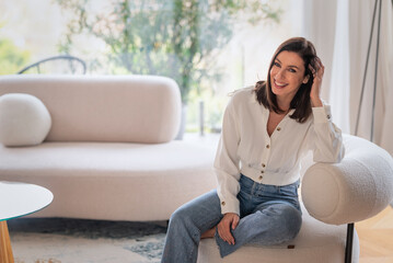 Obraz premium Portrait of an elegant woman relaxing in an armchair in her bright, minimalist home