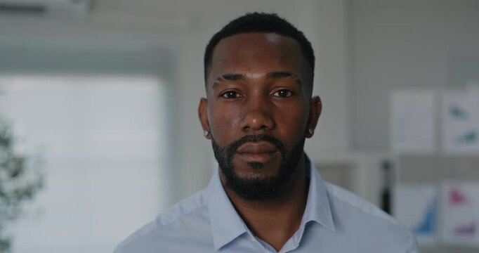 Portrait of African American businessman with beard stands in blue shirt turns head to camera in office. Young manager with confident expression in workplace