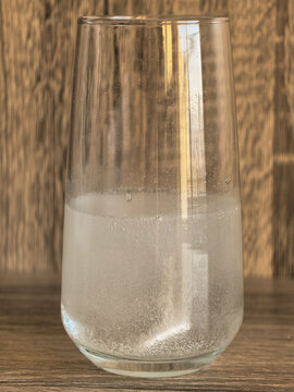 Glass of sparkling mineral water with bubbles on a wooden background. или Effervescent soluble tablet dissolving in a glass of water. 