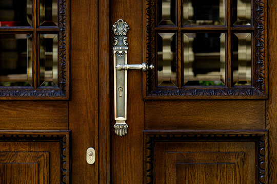 Ornate silver handle on carved wooden doors with glass inserts