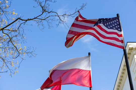 American and Polish flags waving together against a blue sky
