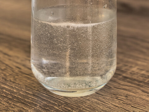 A soluble effervescent tablet in a glass of water on the table.