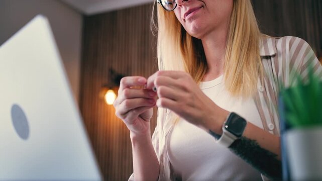 Young professional woman with tattoo and smartwatch starts workday by inserting wireless earphones to join business meeting or webinar on laptop. Remote work, modern digital communication.