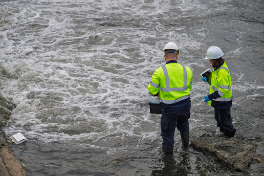 Environmental engineers collecting water samples for laboratory analysis and quality control monitoring near industrial drainage pipes to ensure safety and ecological sustainability standards.