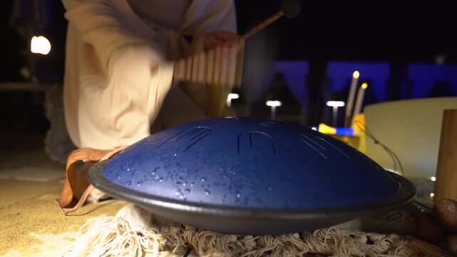 Playing steel tongue drum at night outdoors for meditation and relaxation with blue and warm ambient lighting professional musician performing spiritual music for wellness and zen atmosphere