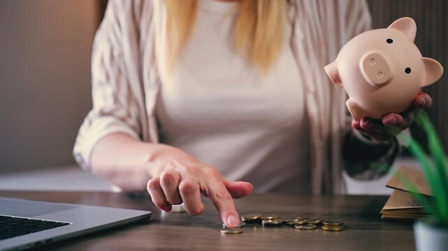 Careful hands empty pink piggy bank and meticulously counting coins on wooden desk, Concept of importance of savings, investment, and financial planning for future
