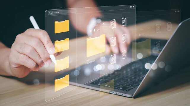 Businessman hands using stylus pen with futuristic virtual document management system and floating digital folders on laptop. Cloud storage, paperless office, and online data organization concept.