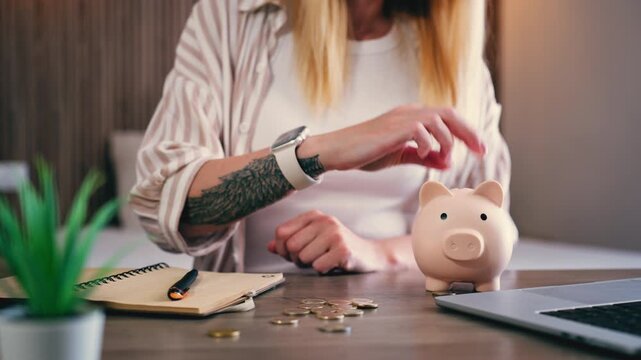 Woman organizes personal finances by tracking monthly budget in notebook and adding coins to piggy bank. Financial discipline, household expense planning and savings management at home concept