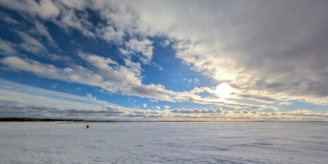 Obraz premium Lone figure stands on vast frozen expanse under dramatic cloudy sky with sunlight peeking through.