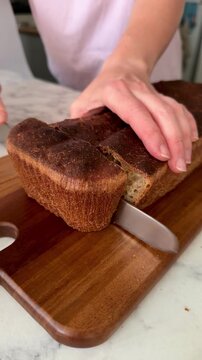Close-up of a female hand cutting artisan sourdough bread on a wooden board. Fresh homemade loaf, rustic kitchen scene