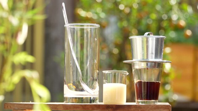 Pouring condensed milk into a large glass for Vietnamese coffee with phin filter background.
