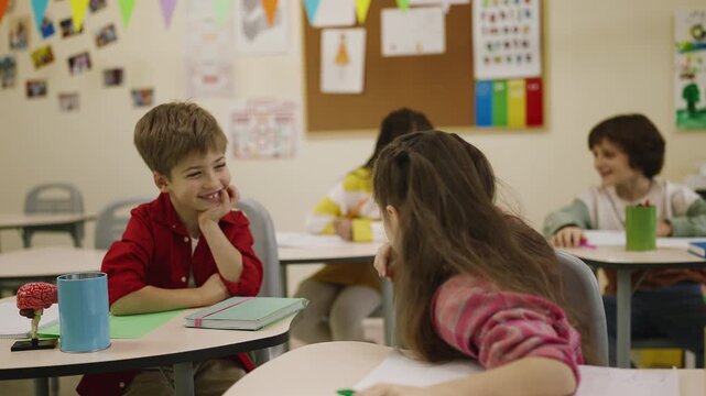 Happy schoolchildren laughing and talking during break in school classroom