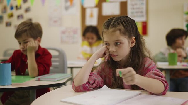 Tired primary school girl feeling bored during classroom lesson, school life