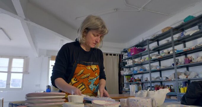 Crafting Pottery: An artist, immersed in the pottery studio, skillfully molds clay, her hands shaping unique forms as she focuses on the task, passion and creativity.