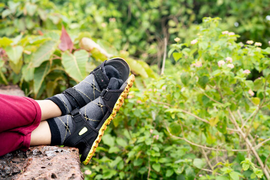 Close-up of person resting legs wearing sandals and socks, set against lush green foliage, conveying relaxation and outdoor leisure vibe.