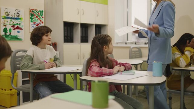 Teacher giving graded papers to happy elementary school students in classroom