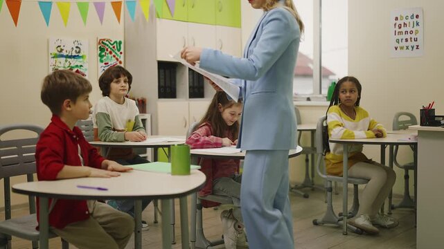 Woman teacher handing graded test papers to elementary school students