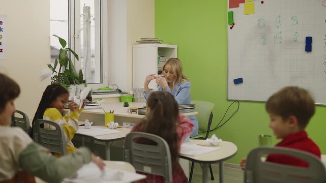 Tired teacher holding head while pupils act noisy and play around in classroom