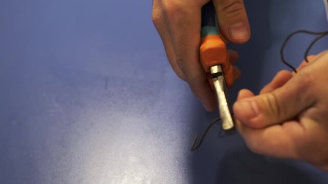 Close-up of male hands bending electrical wire with pliers, shaping cable during repair or installation work, precise manual process using hand tools in workshop or home environment