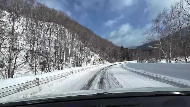 POV dashcam driving on a snowy and icy road in Furano Hokkaido Japan through a winter forest and mountain landscape